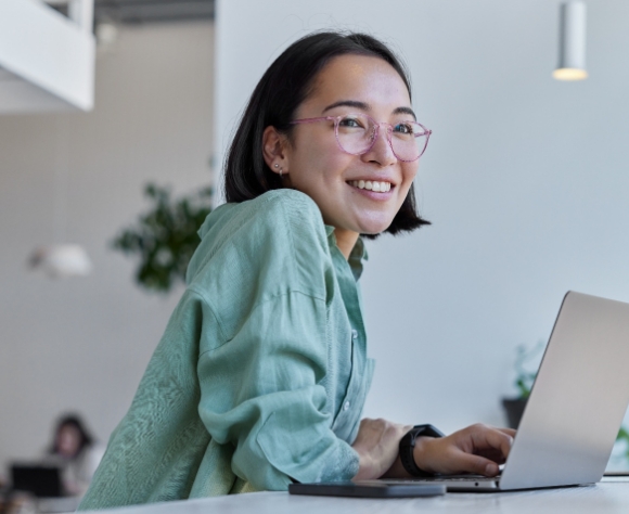 Student with glasses smiling while working on laptop