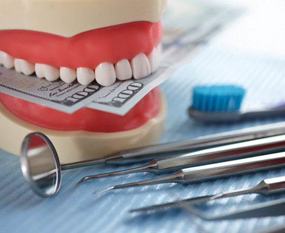 Model of teeth holding money on table of dental instruments